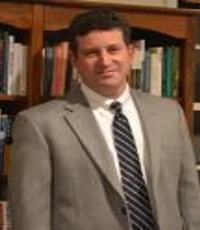 Dr. Alexander Pitofsky in a charcoal grey suit in front of a bookcase